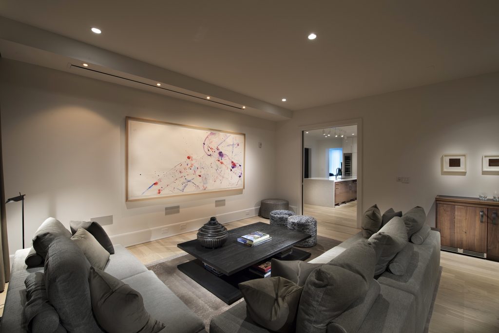 Media room with a ceiling slot for a hidden projection screen and in-wall speakers below a large framed painting in a Midtown Atlanta home